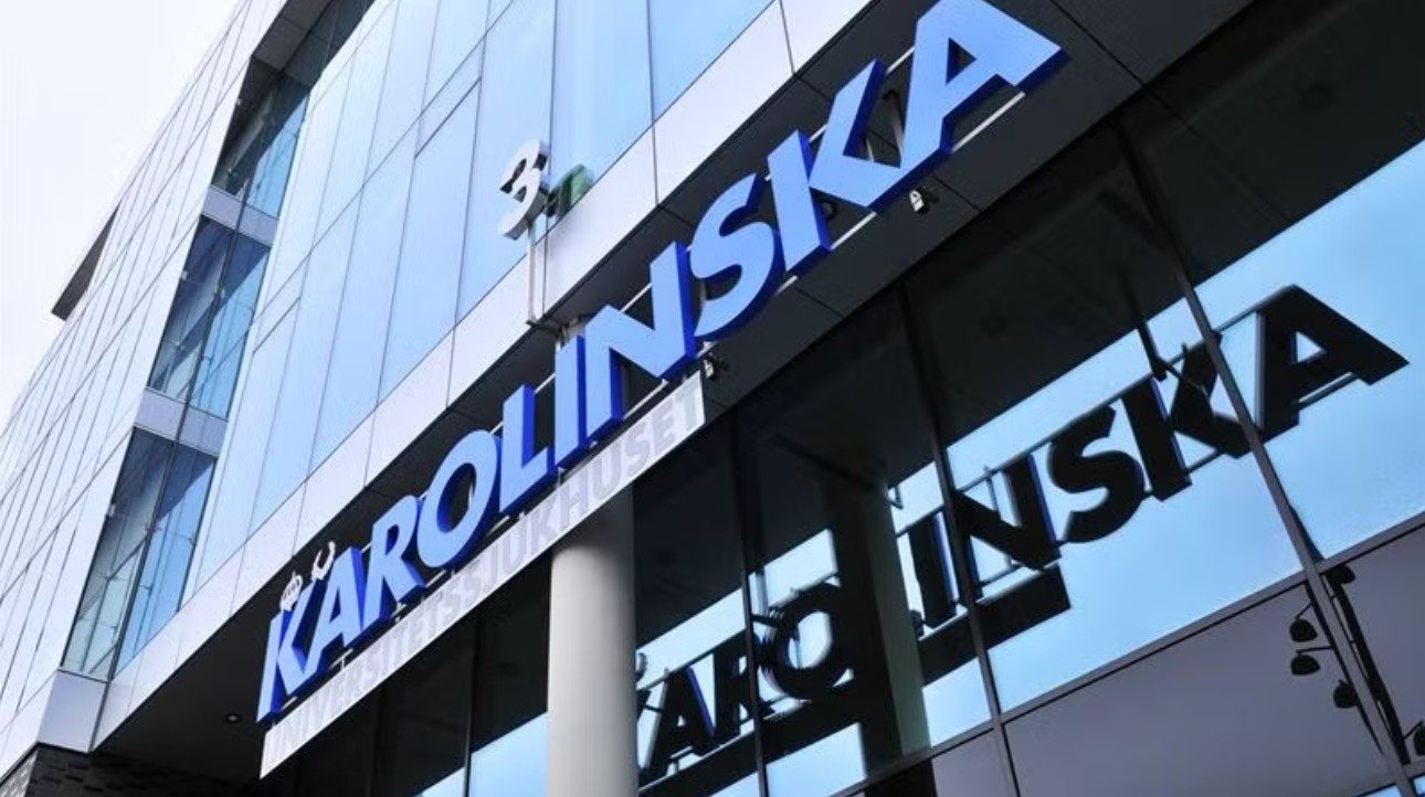 Den moderna entrén till Karolinska Universitetssjukhuset, med stora upplysta bokstäver som bildar texten "KAROLINSKA" på en glasfasad.